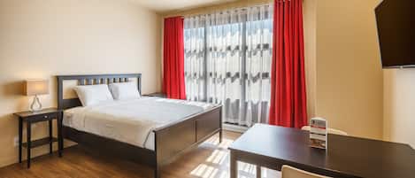 Una habitació d'hotel amb llit, taula de nit, làmpada i escriptori amb cadira.