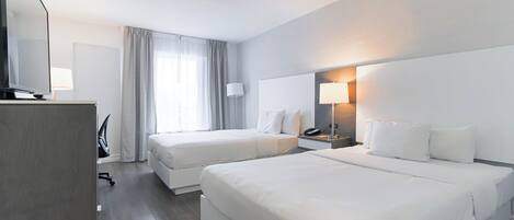 Een hotelkamer met twee bedden, een bureau met stoel, een televisie en een lamp.