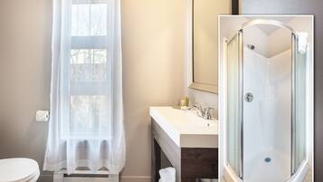 A bathroom with a toilet, a sink, a shower, and a window with a sheer curtain.