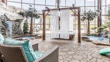 Relax in a serene garden oasis with a hot tub, waterfall, and comfortable seating under a shaded pergola.