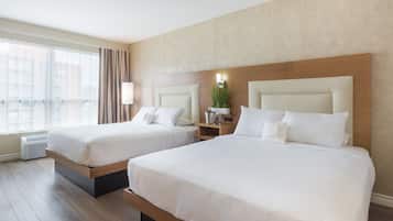 Habitación de hotel con dos camas, un ventanal con cortinas, una mesita de noche con lámpara y una planta en la pared.