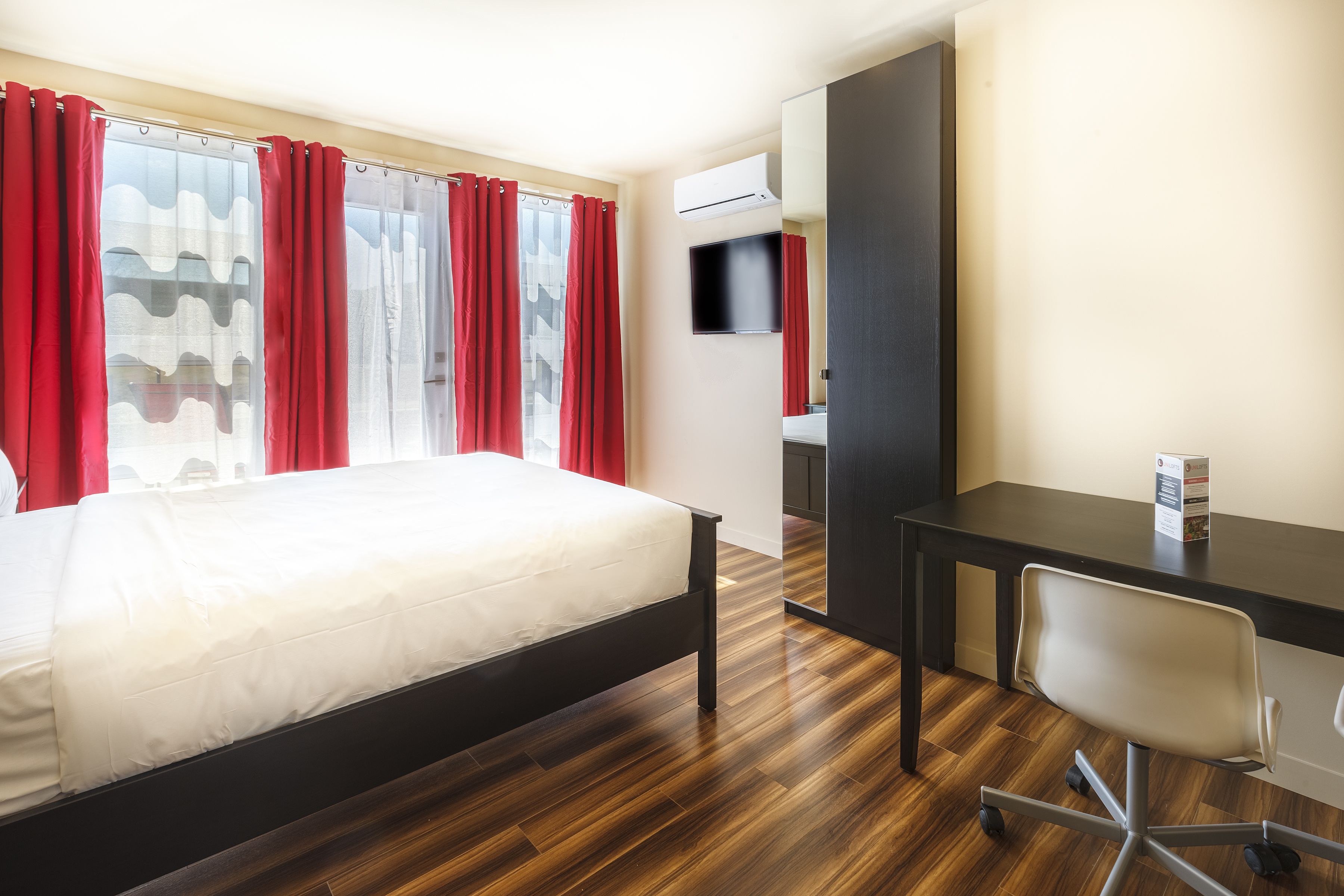 A hotel room with a bed, a desk, a chair, and a TV.