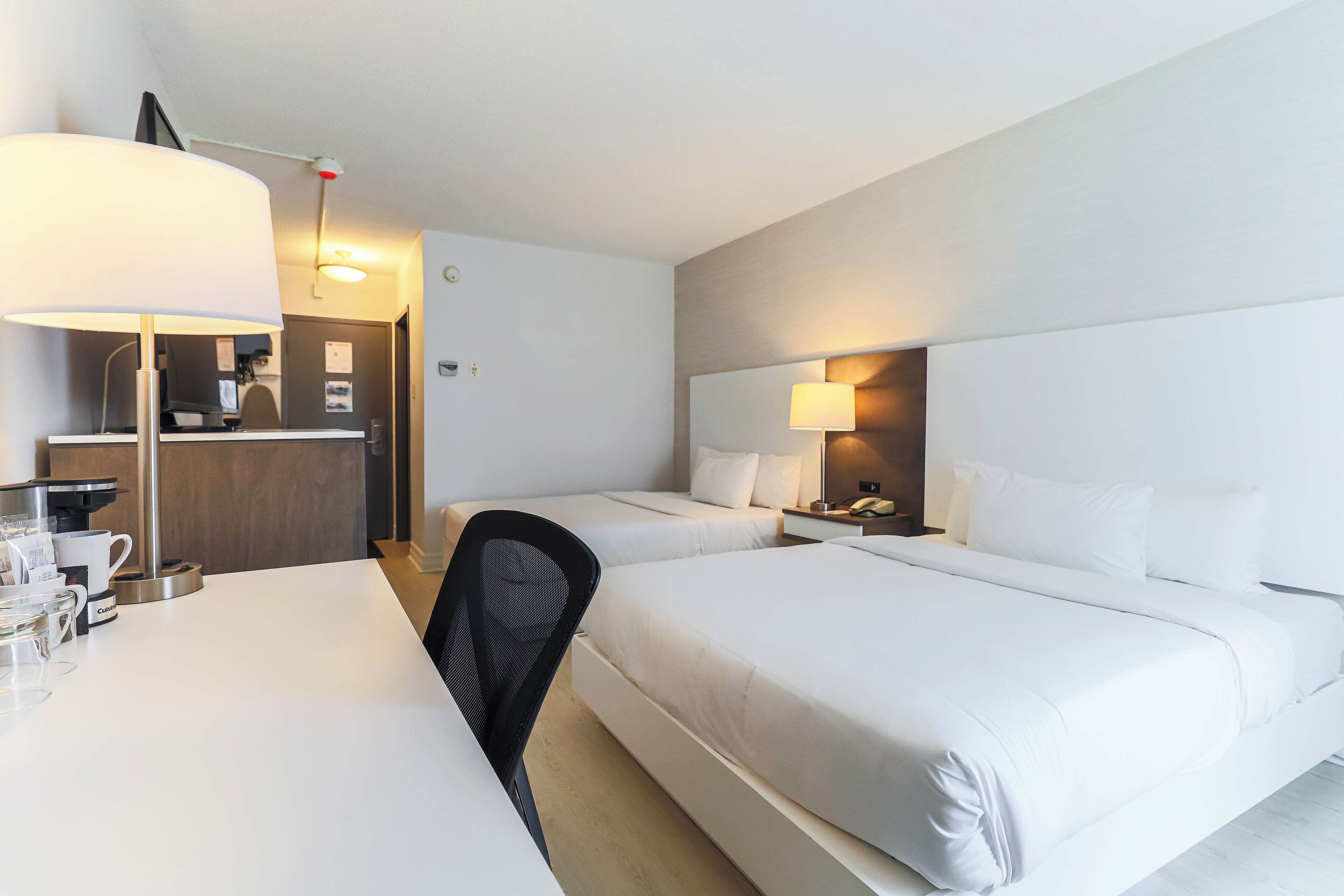 Une chambre d’hôtel avec deux lits, un bureau équipé d’une machine à café et une chaise.