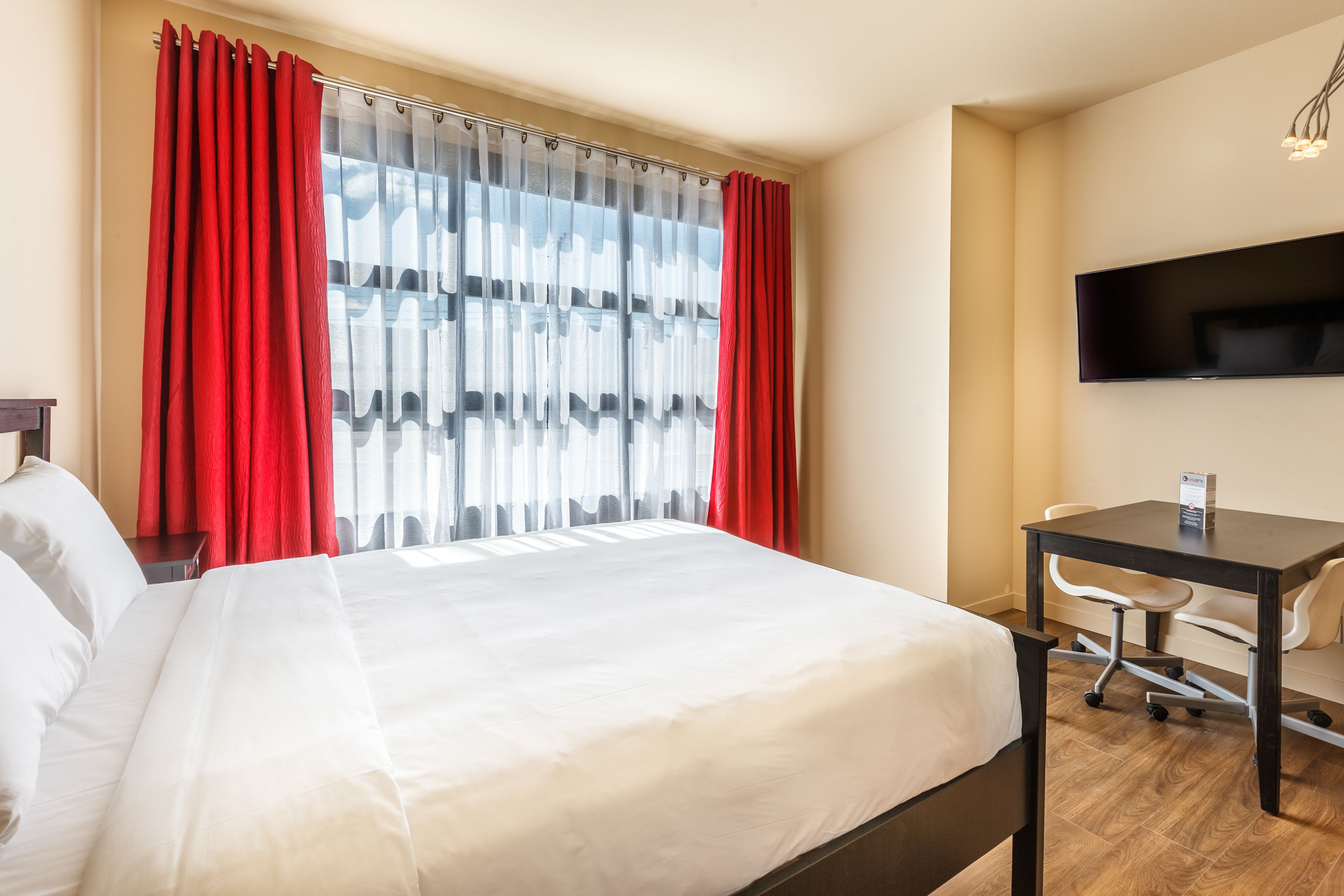A hotel room with a bed, a desk, a chair, and a TV mounted on the wall.