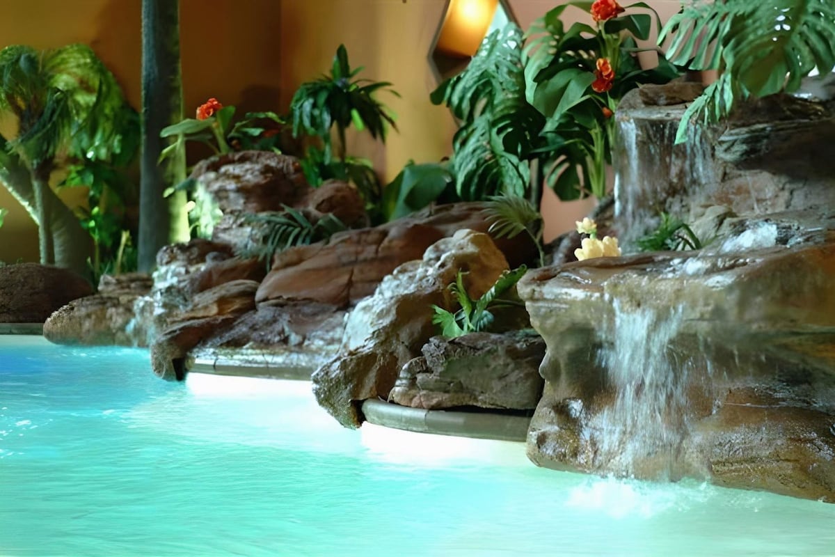 A pool with a waterfall feature surrounded by rocks and tropical plants.