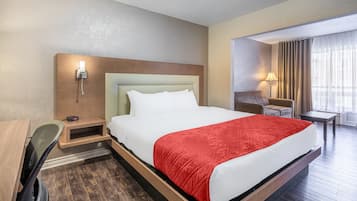 Ein Hotelzimmer mit Bett, Schreibtisch, Stuhl, Nachttisch, Lampe und einem Fenster mit Vorhängen.