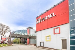 A modern hotel building with a prominent red and white facade, large glass windows, and a covered entrance area. - Hotel Universel (Québec City)