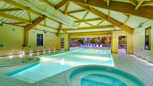 Una piscina interior con techo de madera y paredes de azulejos, rodeada de sillones de descanso y vistas al exterior.