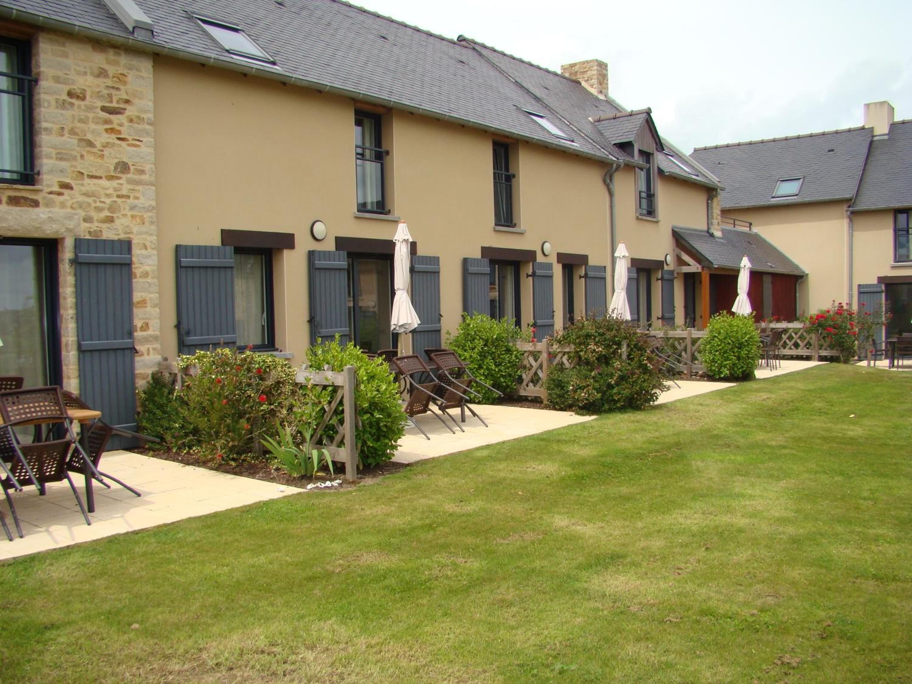A row of rooms with shutters, outdoor seating, and a well-maintained lawn.