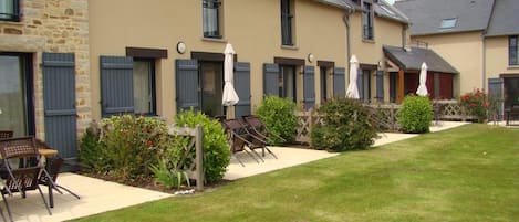 A row of rooms with shutters, outdoor seating, and a well-maintained lawn.