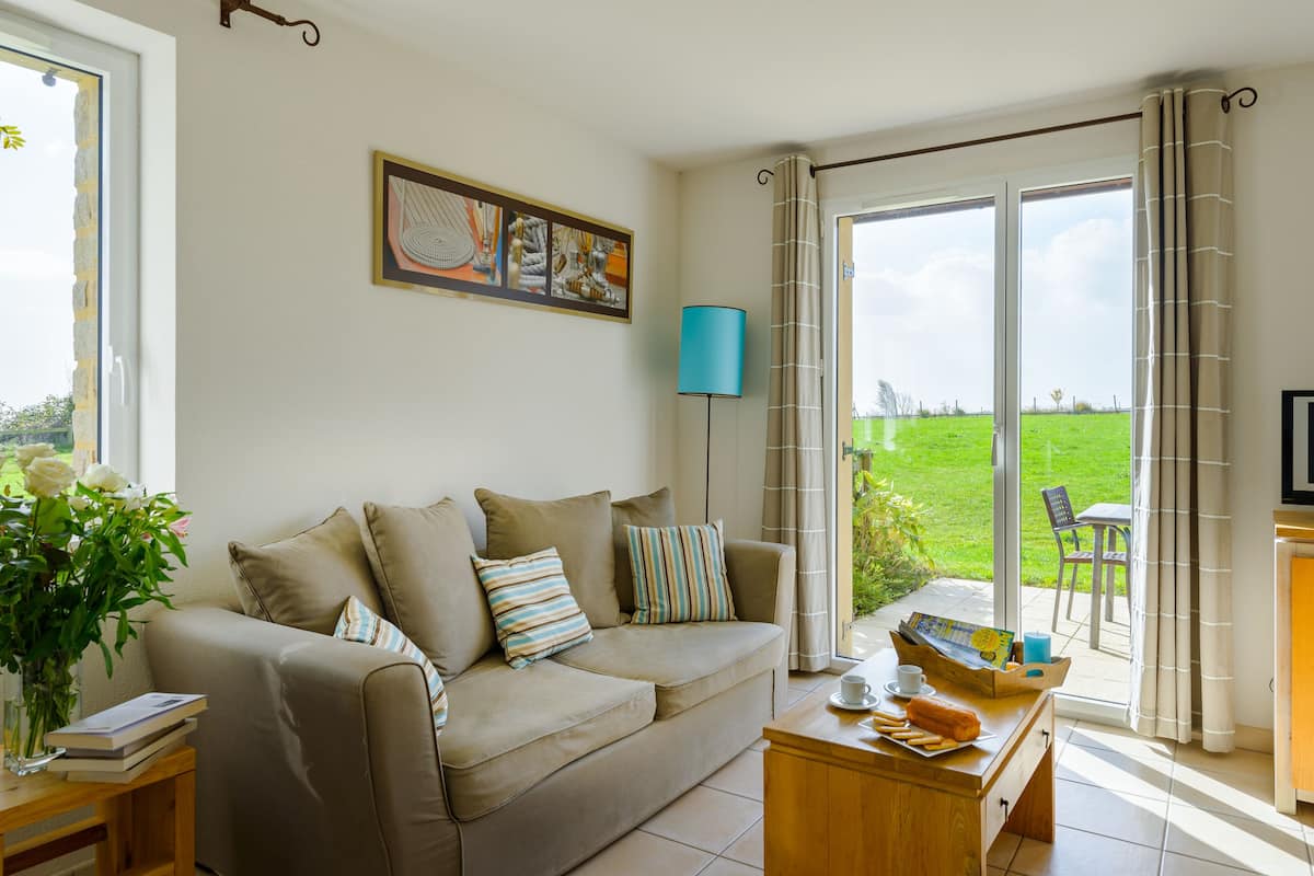 A living room with a sofa, a coffee table, a TV, and a view of a green lawn through a sliding door.