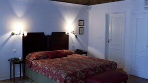 A bedroom with a bed, two bedside lamps, a wooden headboard, a door, and a patterned rug. - Hotel Riviera (Évora)