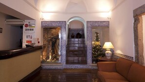 A lobby with a reception desk, a staircase, a Christmas tree, and a statue. - Hotel Riviera (Évora)