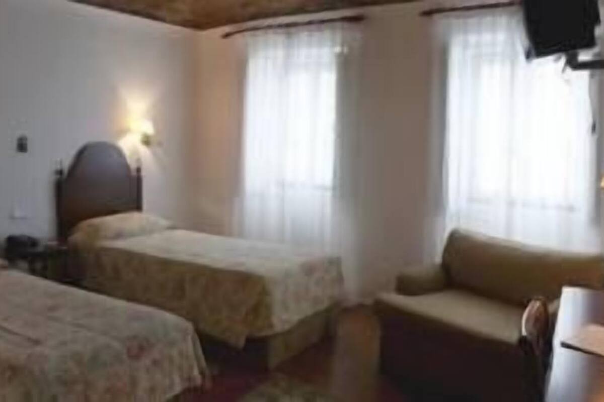 Hotellihuone, jossa on kaksi erillistä sänkyä, sohva, työpöytä ja ikkuna, jossa on verhot.