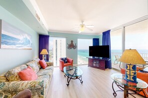 A living room with a sofa, coffee table, and TV, with a balcony and ocean view.