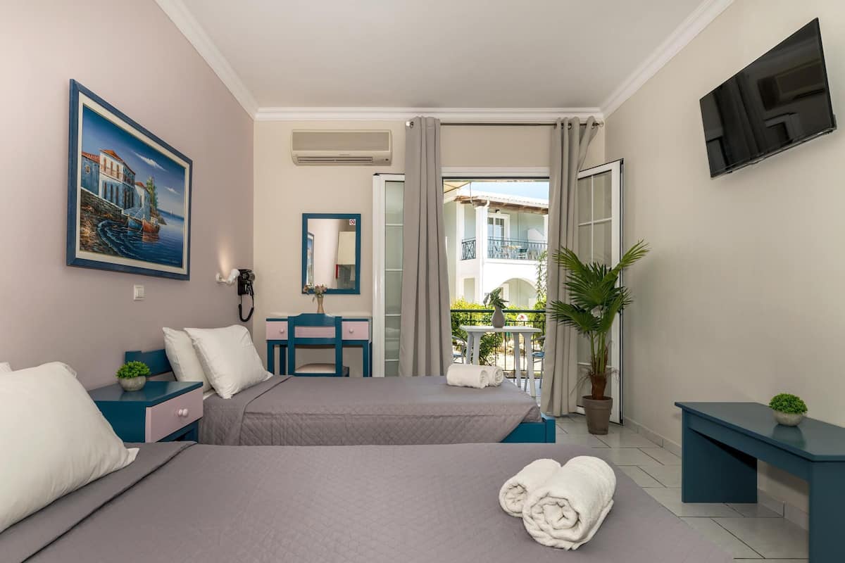 Ein Hotelzimmer mit zwei Betten, einem Schreibtisch, einem Sessel und einem Balkon mit Blick, sowie einem Bild an der Wand.