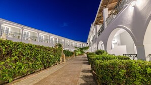 Un patio con un sendero de piedra bordeado por setos cuidados y edificios blancos con balcones.