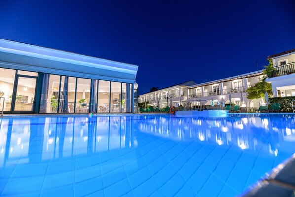 A swimming pool with a modern building adjacent to it, featuring large windows and outdoor seating.