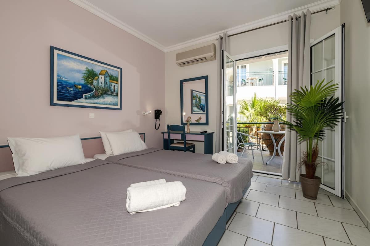 Ein Hotelzimmer mit Bett, Schreibtisch, Stuhl, einer Zimmerpflanze und einem Balkon mit Sitzmöbeln.