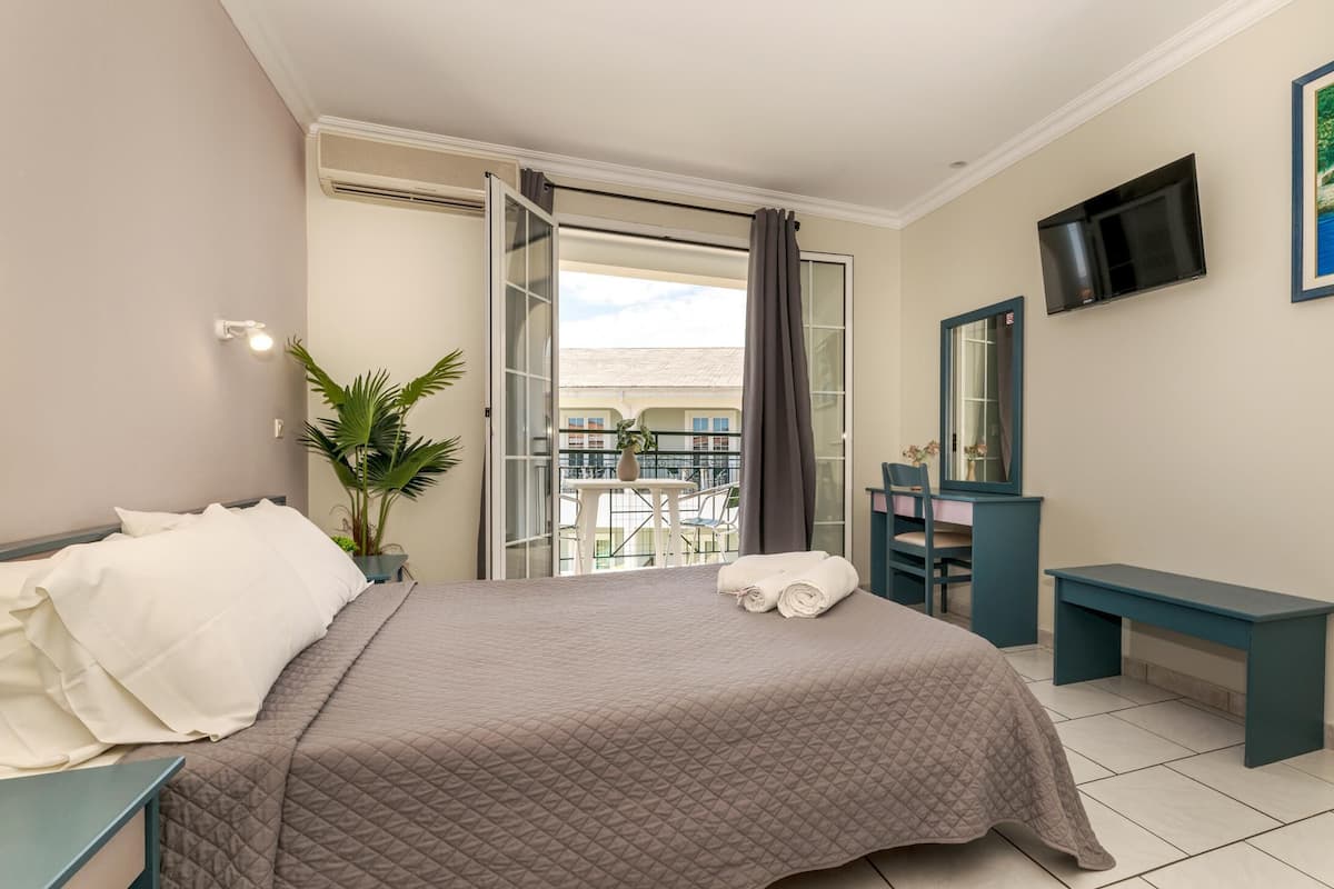Ein Hotelzimmer mit Bett, Schreibtisch, Stuhl, Fernseher und einem Balkon mit Blick auf Gebäude.