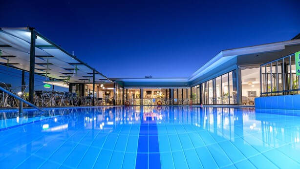 Una amplia piscina interior con paredes de vidrio transparente, un diseño arquitectónico moderno y un interior bien iluminado.