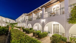 Un patio con edificios blancos, paseos con arcos y vegetación.