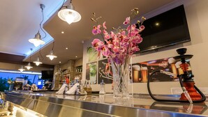 Una zona de bar con una barra larga, un narguilé y un jarrón de orquídeas rosadas.