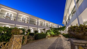 Un hotel de varios pisos con balcones, jardineras de piedra y un sendero pavimentado.