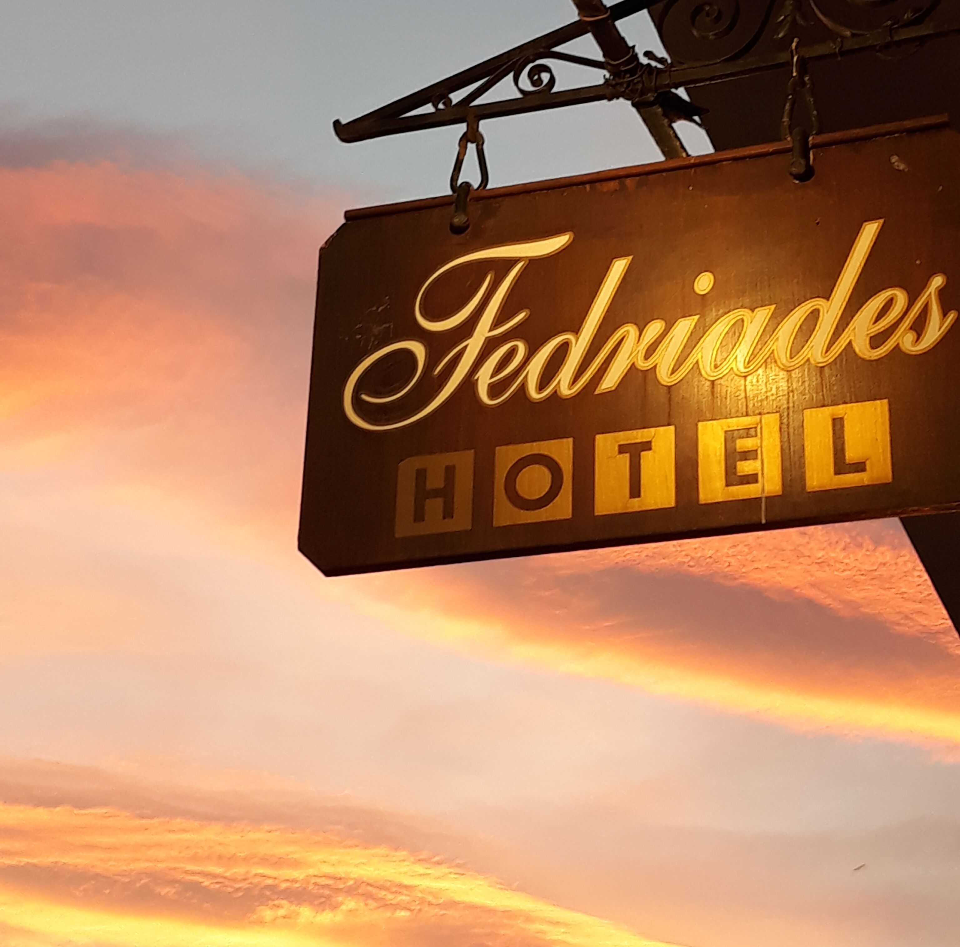 A hotel sign with the name "Fedriades Hotel" against a sunset sky.
