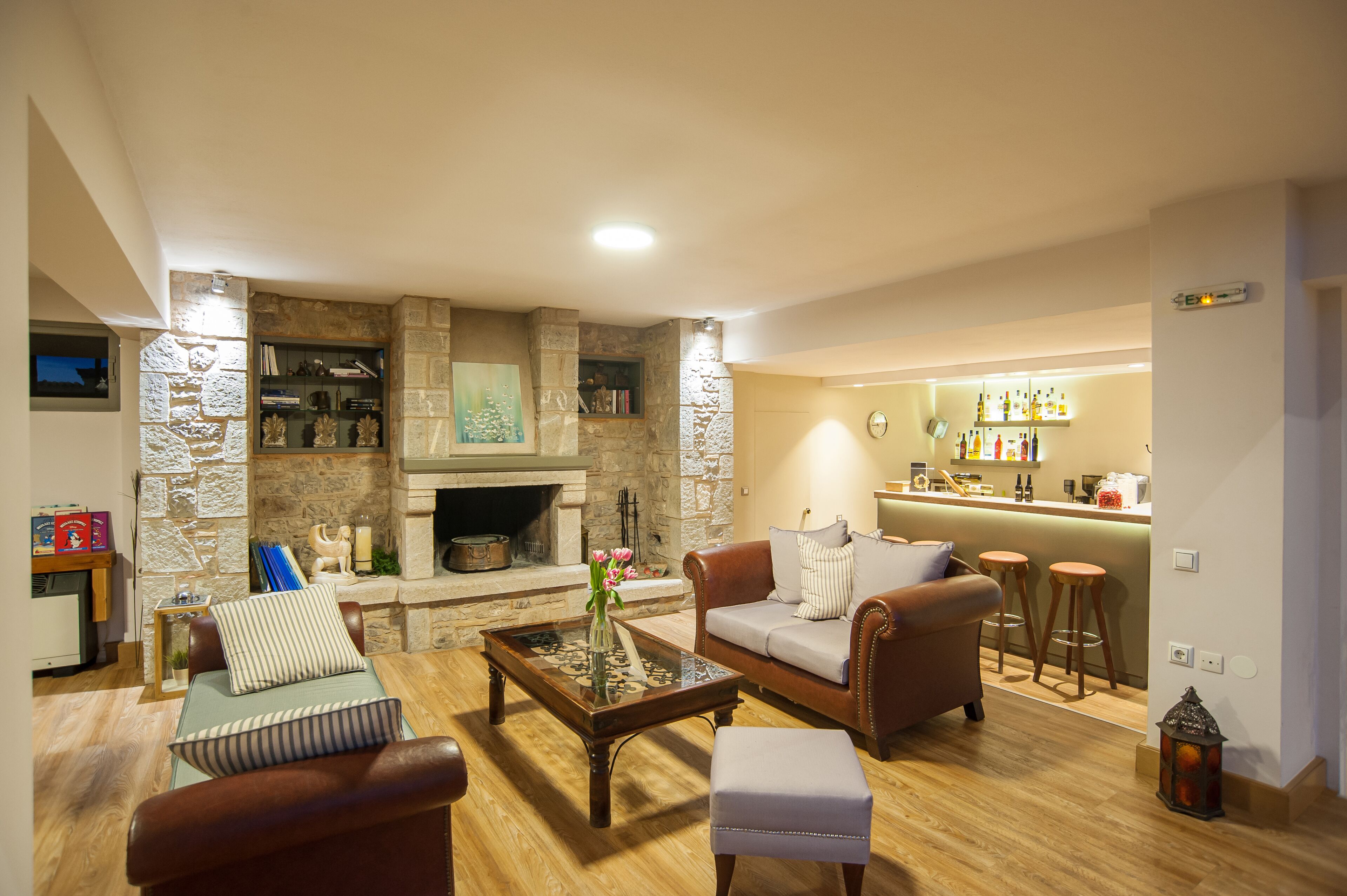 A cozy living room with a stone fireplace, leather sofas, a coffee table, and a bar area with stools.