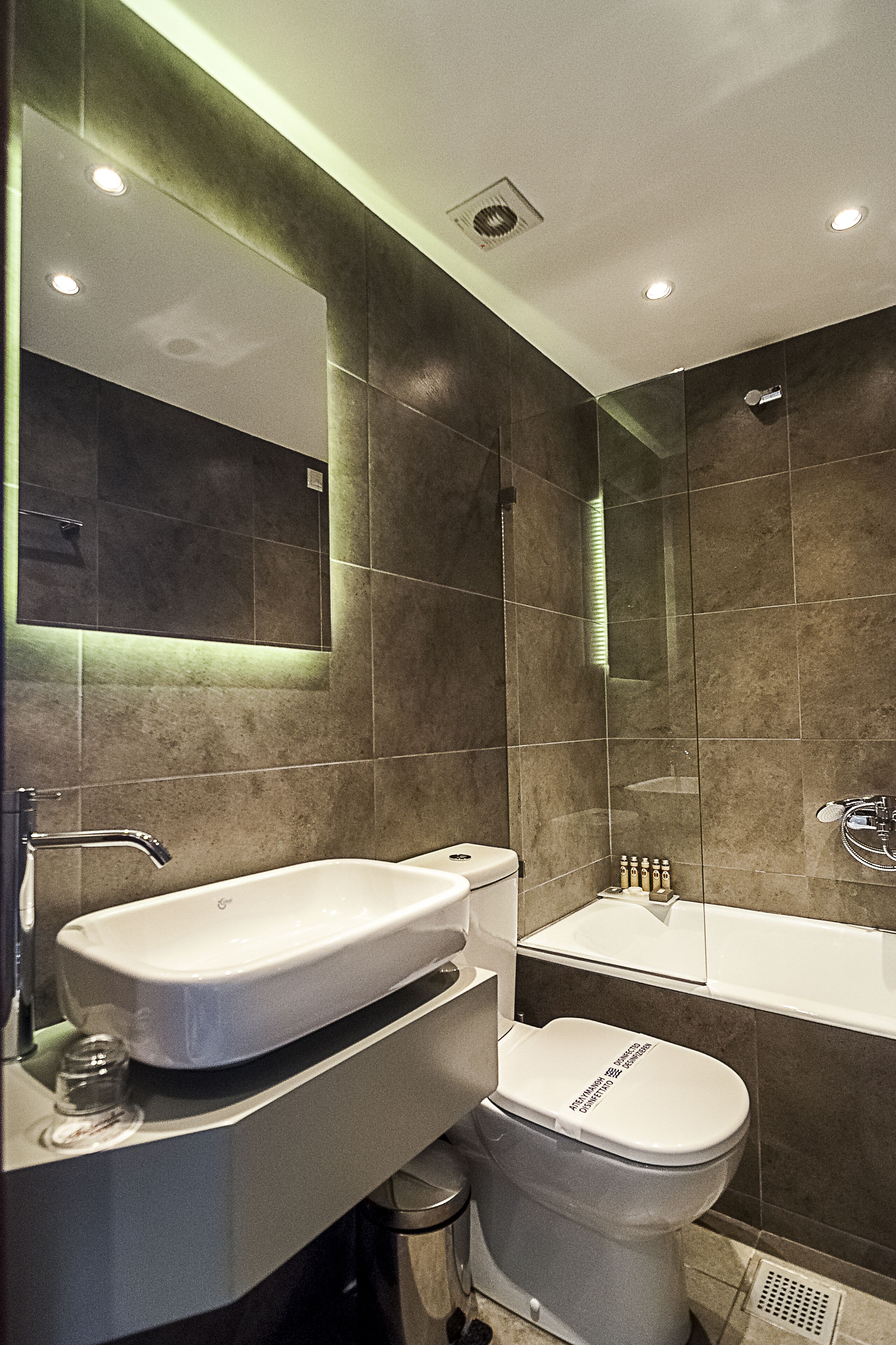 A modern bathroom with a large mirror, a white sink, and a toilet.