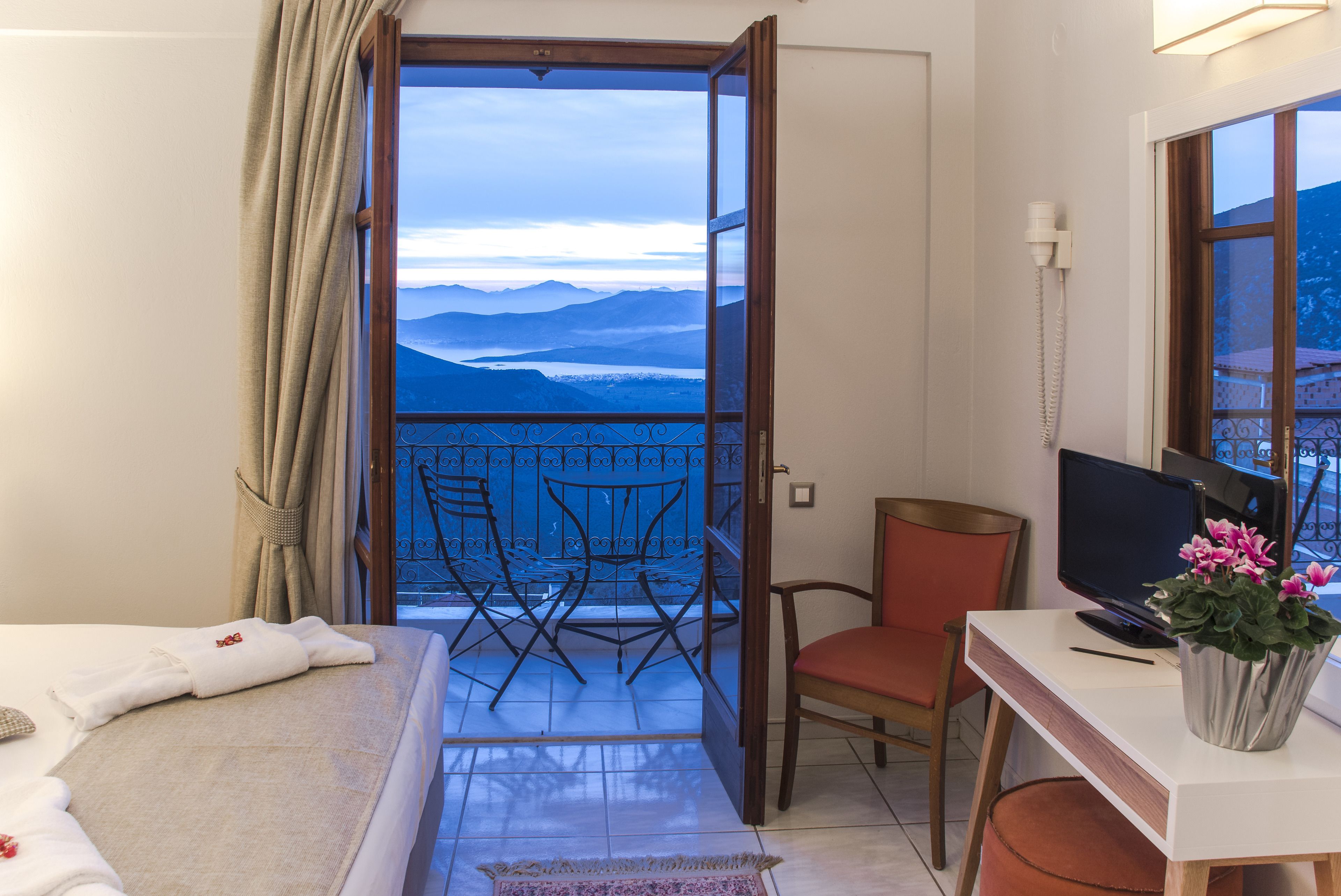 A hotel room with a balcony, a desk with a computer, a chair, and a bed with a neatly made bedspread.
