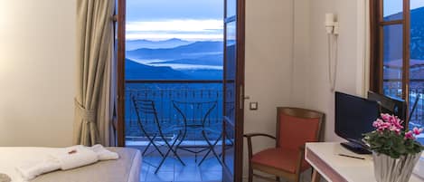 A hotel room with a balcony, a desk with a computer, a chair, and a bed with a neatly made bedspread.