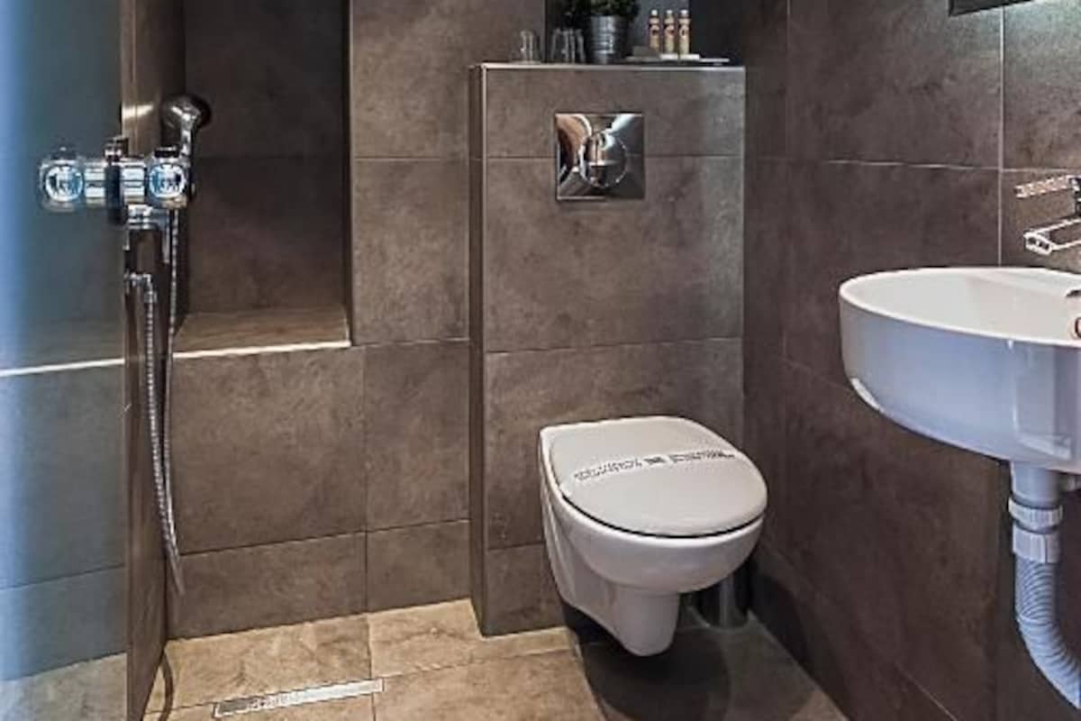 A modern bathroom with a shower, toilet, and sink, featuring dark tiles and a sleek design.