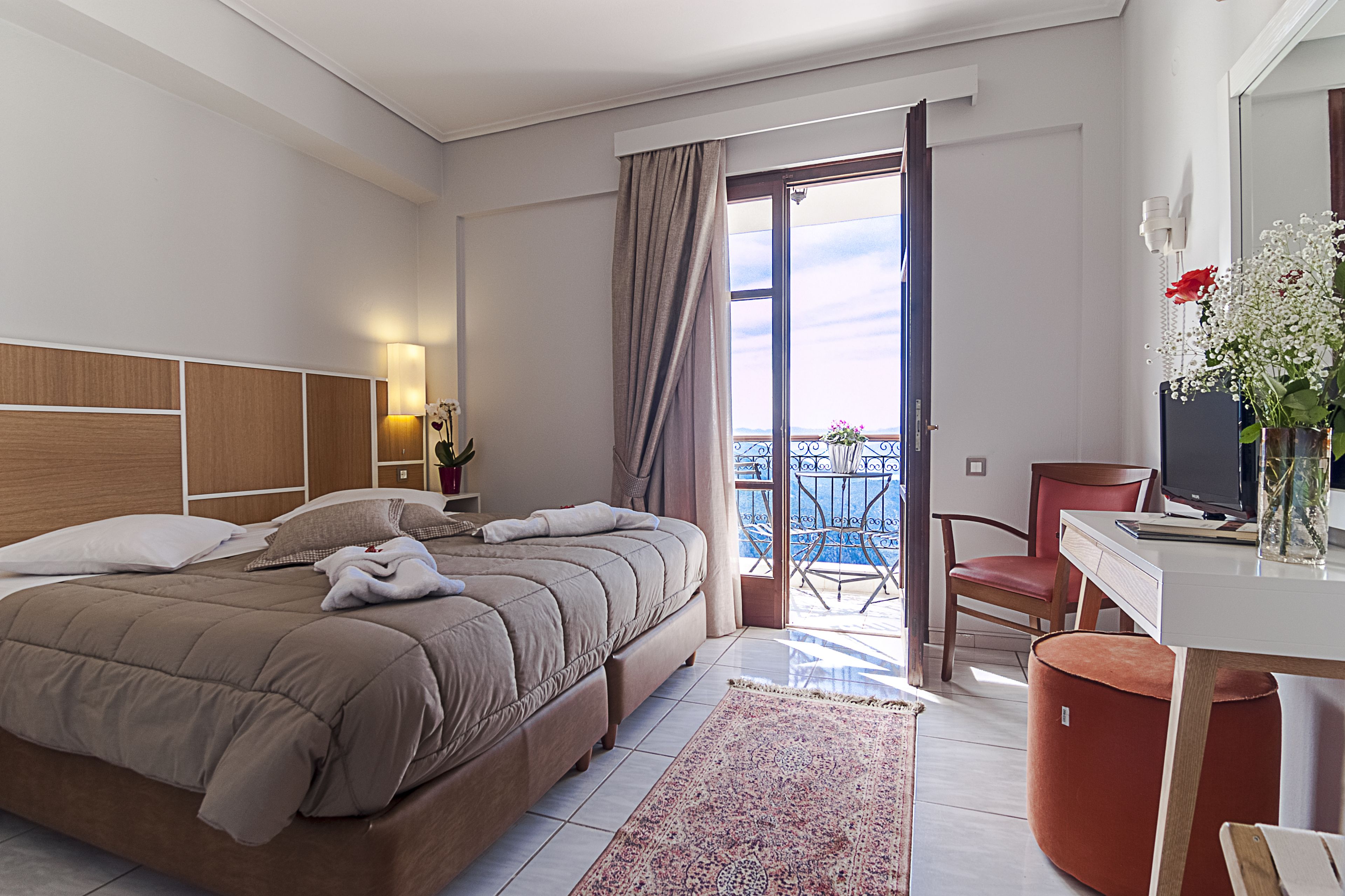 A hotel room with a bed, a desk, a chair, a TV, and a balcony with a view.