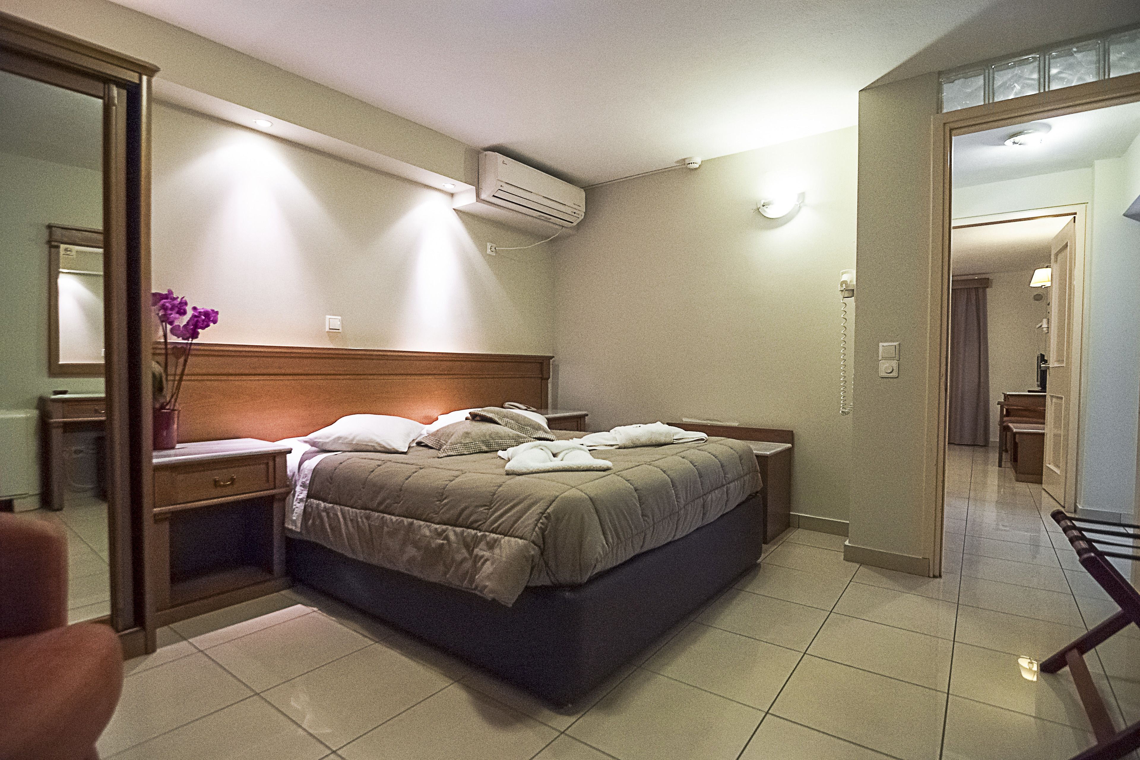 A hotel room with a bed, bedside tables, a mirror, and an air conditioning unit.