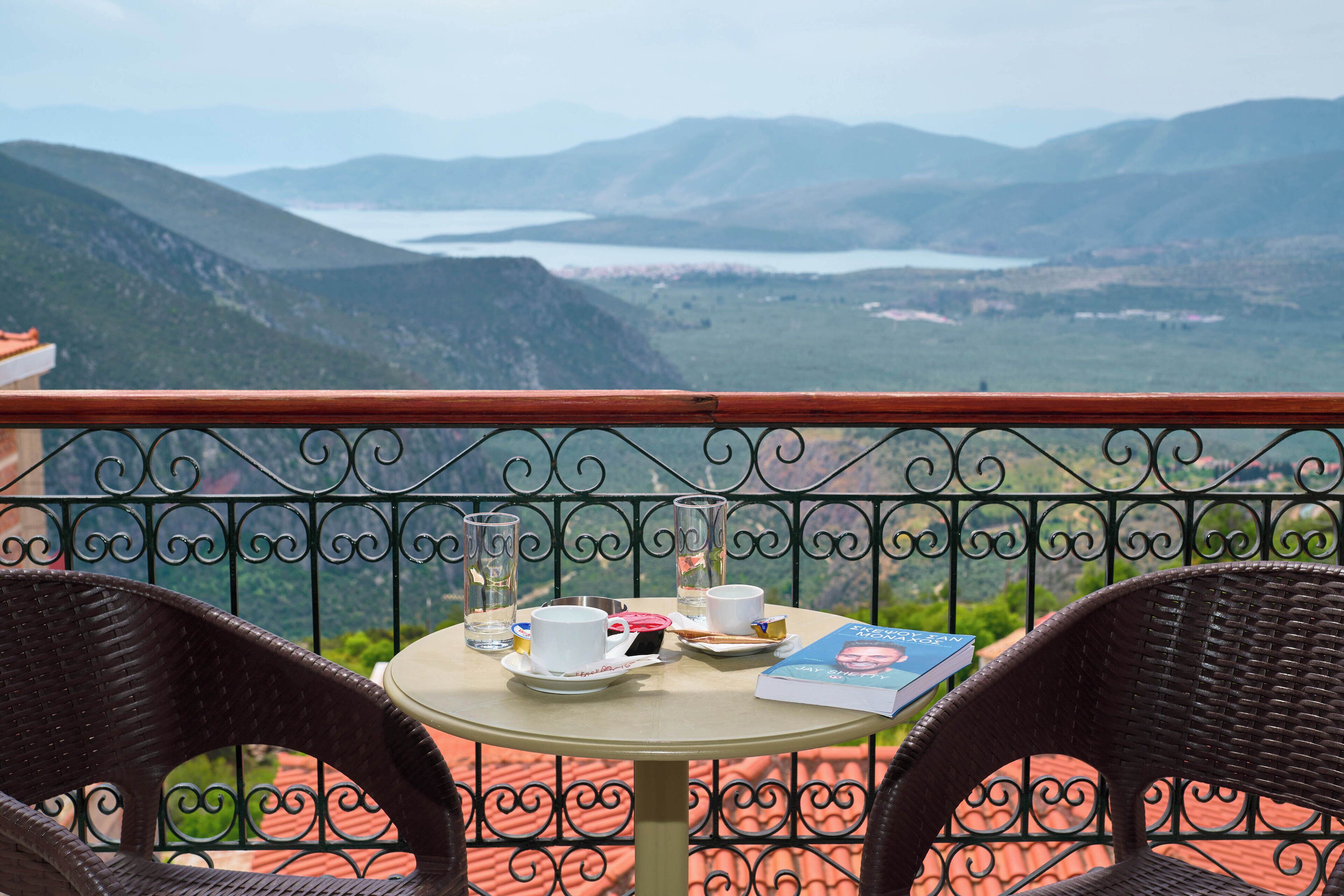A balcony with wicker chairs, a table with a book, cups, and a glass of water.