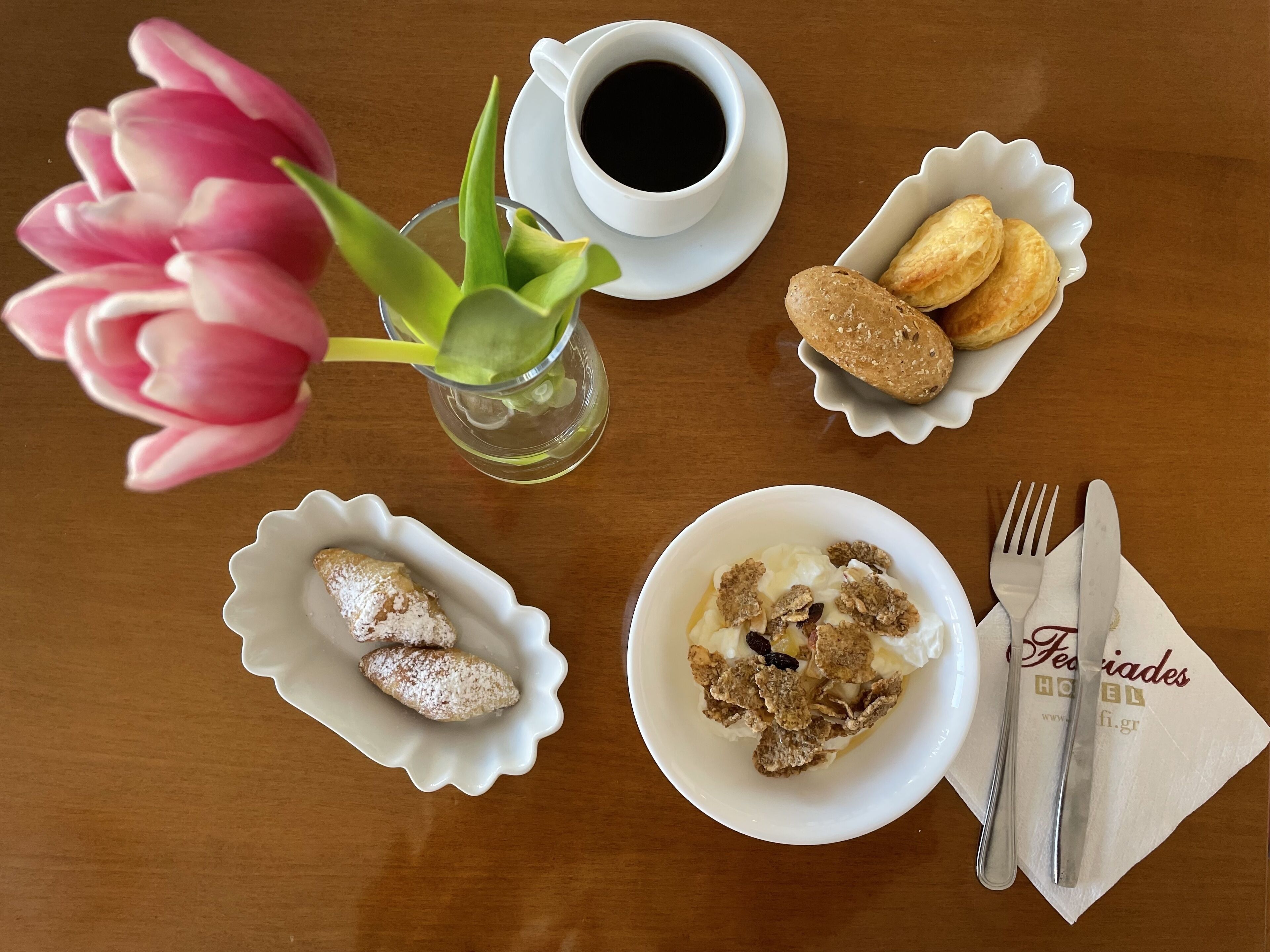 Een tafel met een koffiekopje, gebak, een kom cornflakes en bestek.