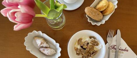 A table with a cup of coffee, pastries, a bowl of cereal, a flower, and cutlery.