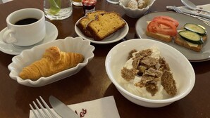 Une table dressée pour le petit-déjeuner, avec des croissants, du pain, du yaourt et des fruits, ainsi qu’un vase de tulipes, du jus et du café.