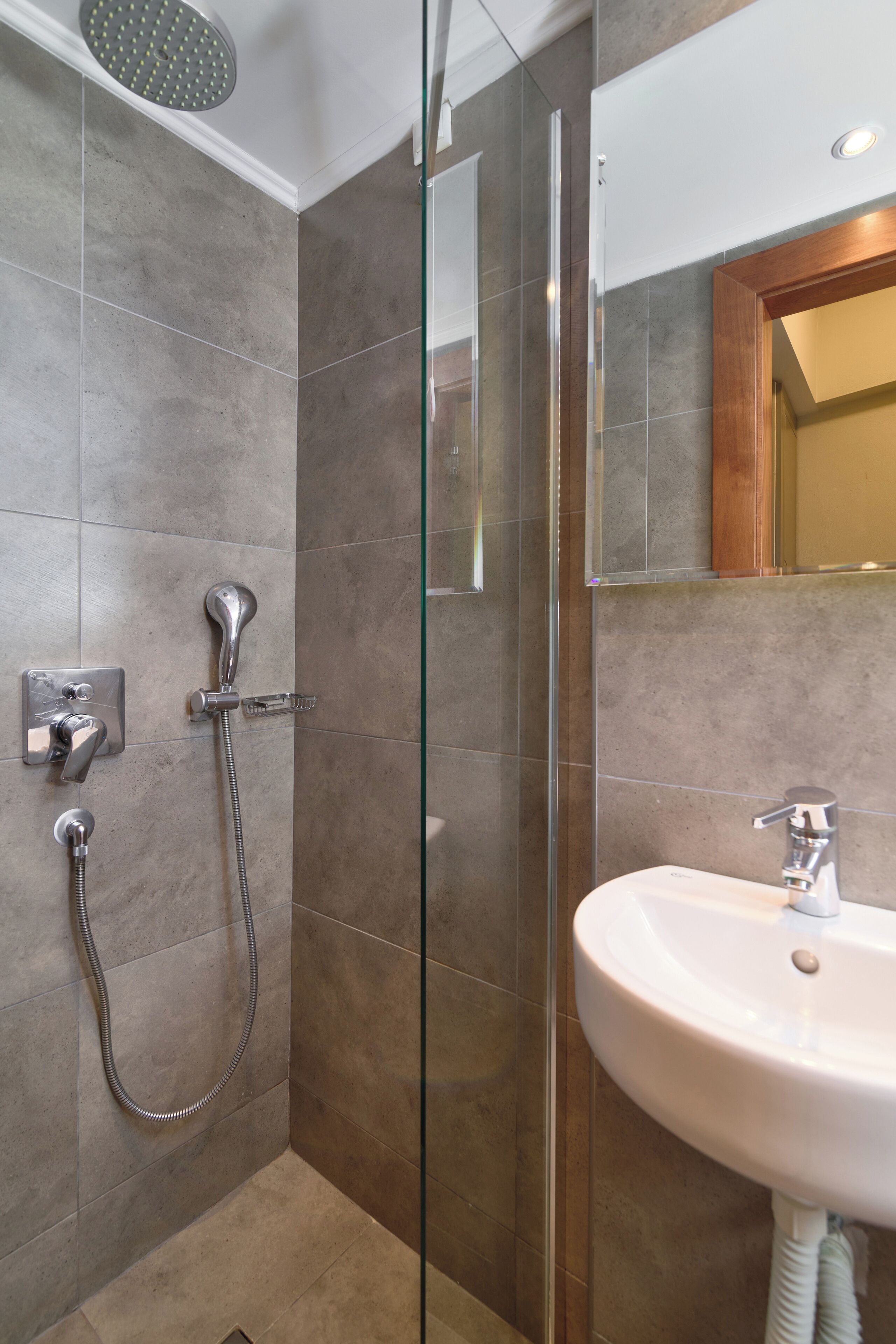 Un baño moderno con ducha envuelta en vidrio, un lavamanos blanco y un espejo sobre el lavamanos.