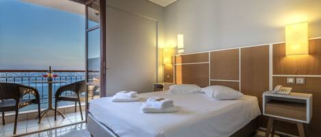 A hotel room with a bed, bedside table, lamp, and a view of the sea.