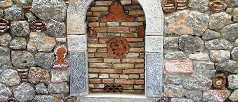 Un muro de piedra con un ventanal de arco, que presenta un diseño de ladrillo y elementos metálicos decorativos.