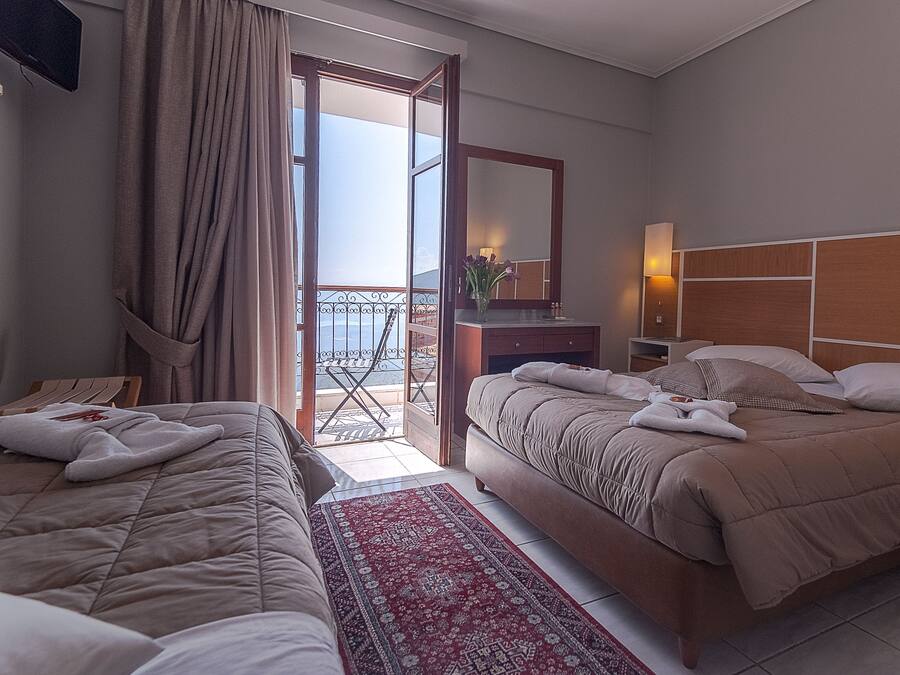 A hotel room with two beds, a red patterned rug, a balcony with a view, and a wooden headboard.