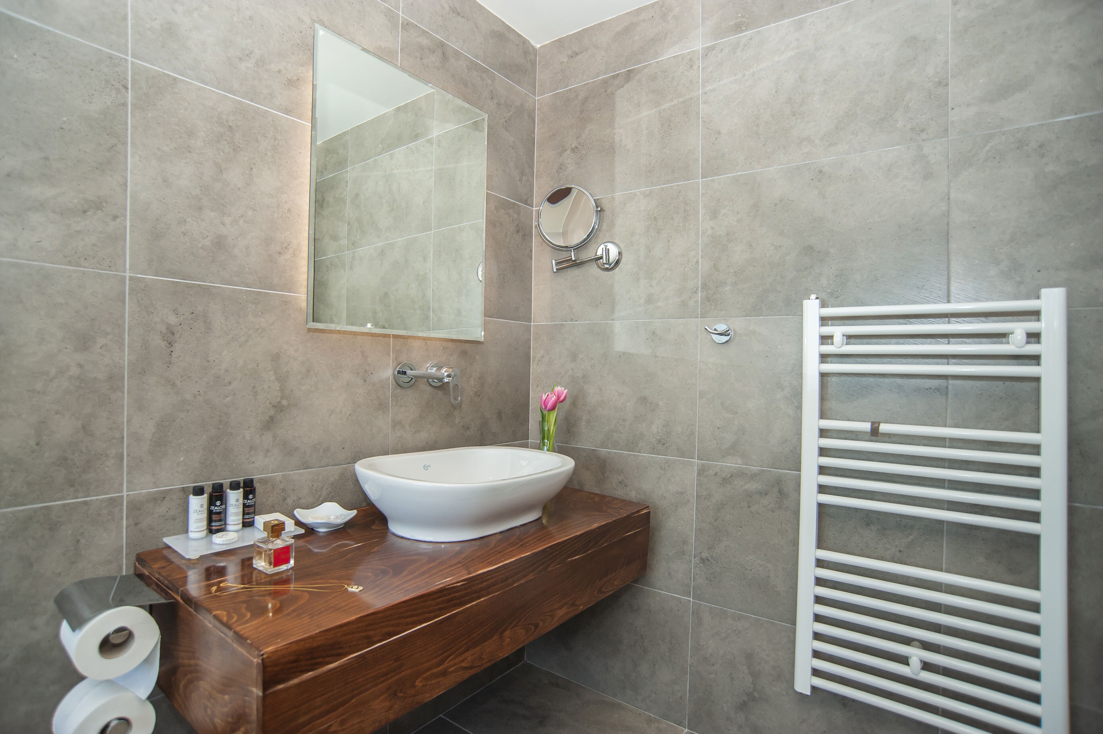 A modern bathroom with a wooden vanity, a white sink, a mirror, and a towel rack.