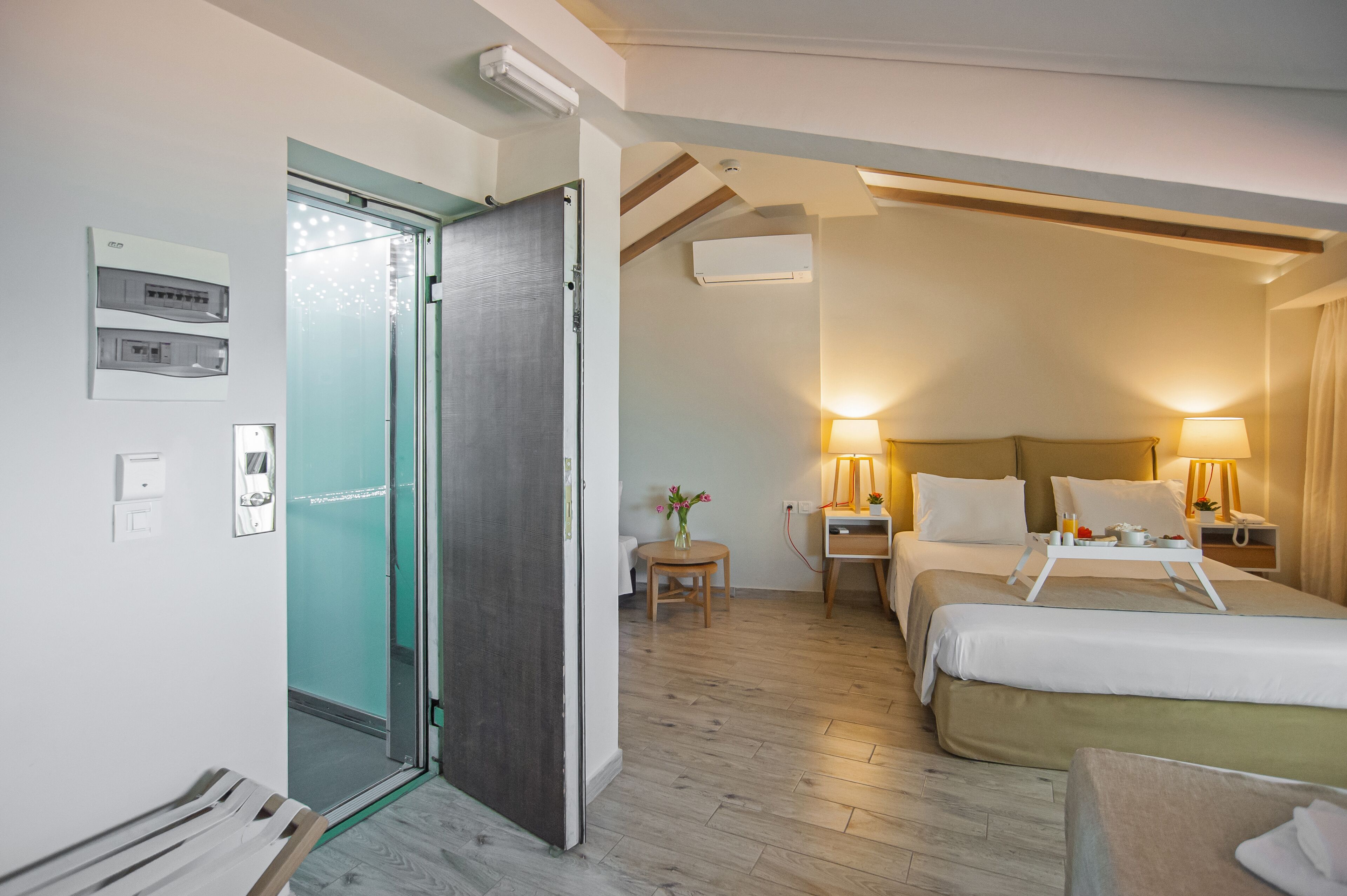 A hotel room with a bed, bedside tables, a lamp, a small table with a vase, and a door leading to a bathroom.