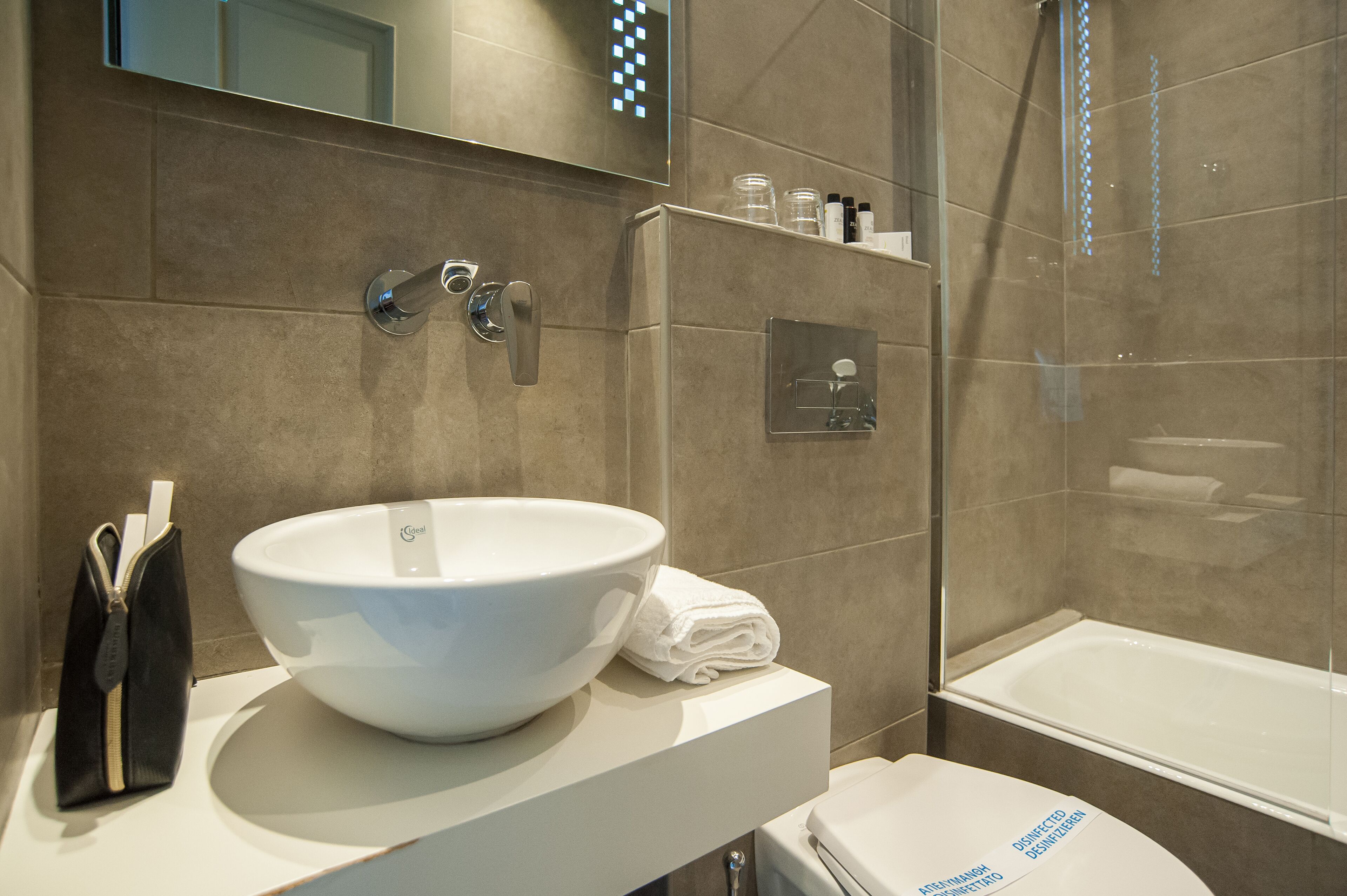 A modern bathroom with a large white sink, a handheld showerhead, and a glass-enclosed bathtub.