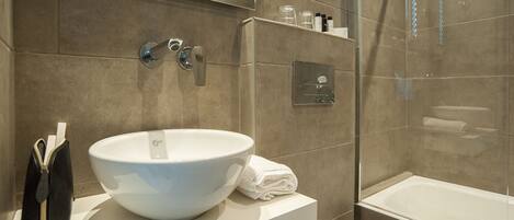 A modern bathroom with a large white sink, a handheld showerhead, and a glass-enclosed bathtub.