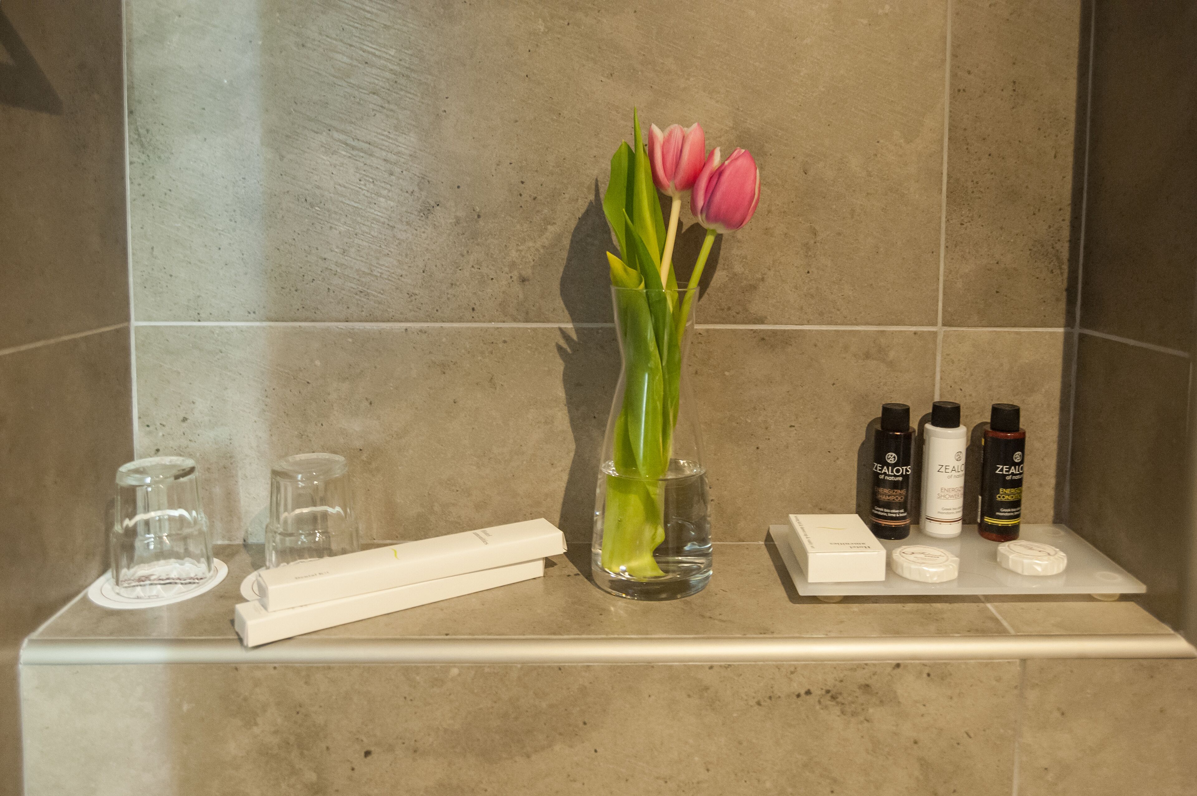 A bathroom vanity with a vase of pink tulips, a toothbrush, and toiletries.