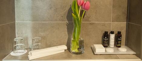 A bathroom vanity with a vase of pink tulips, a toothbrush, and toiletries.